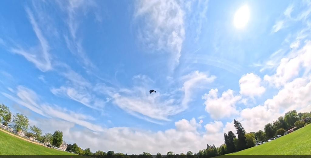 Drone in flight against a wide blue sky with green fields